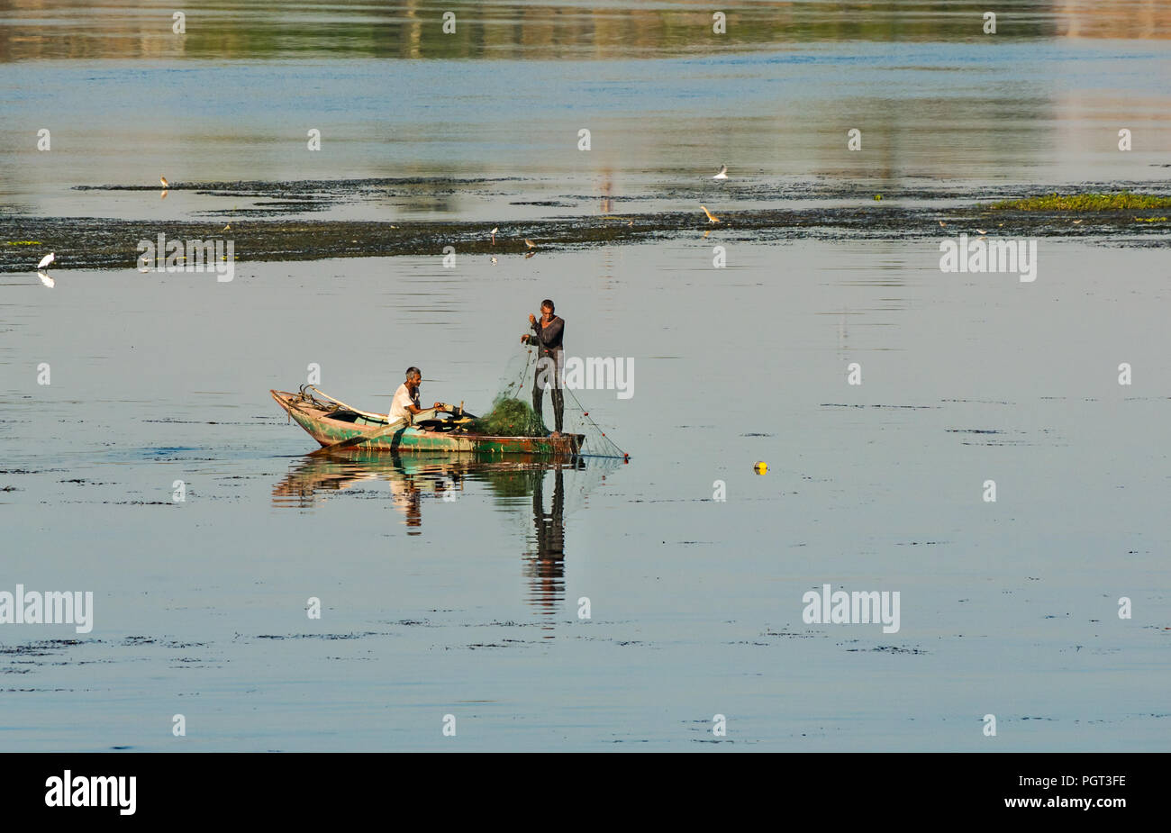 Locale egiziano gli uomini nella vecchia barca a remi di pesca con rete in mattina presto luce, con riflessioni di acqua, Fiume Nilo, Egitto, Africa Foto Stock