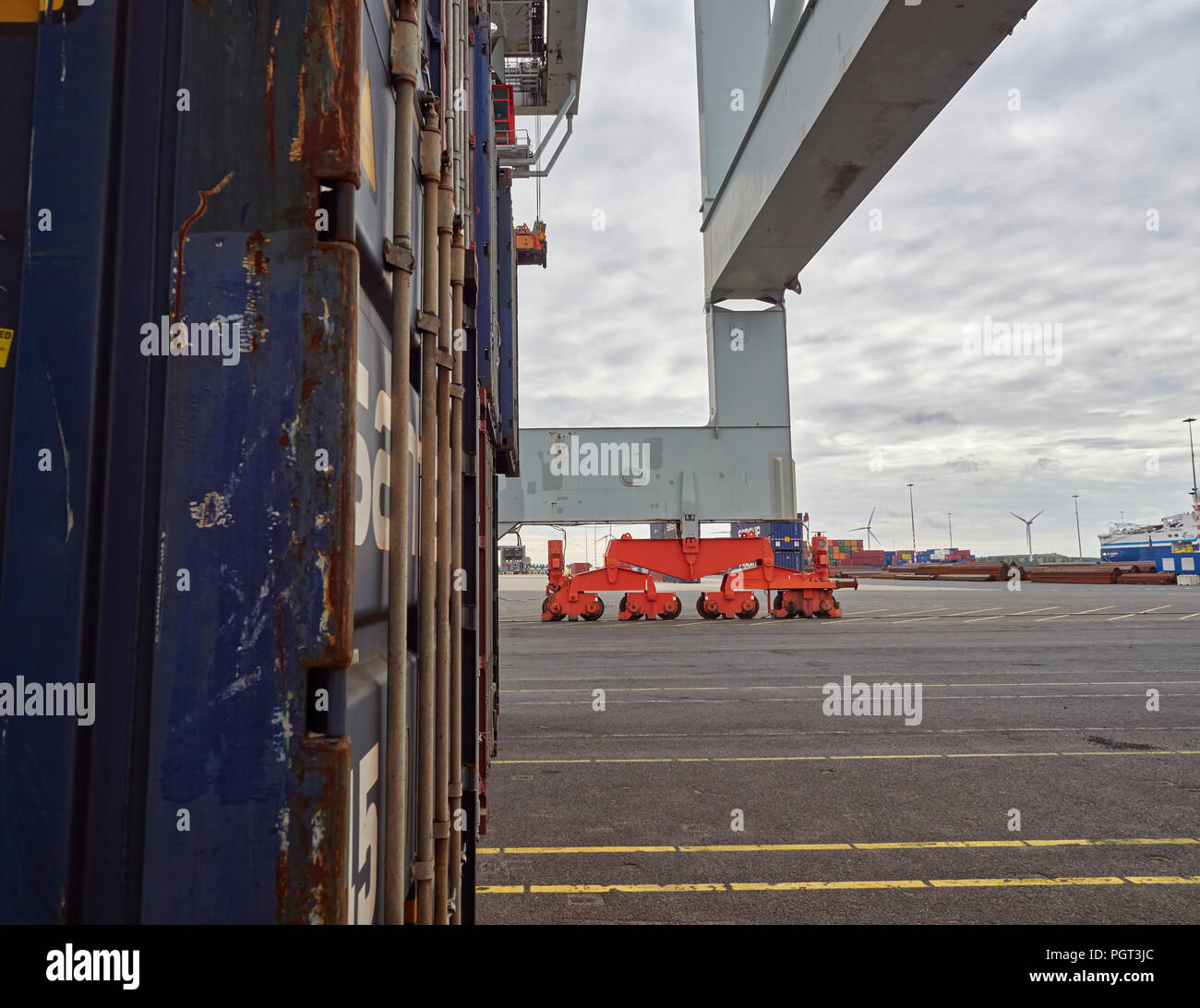 Il rosso carrelli a ruote e della gamba di un contenitore grande gru, accanto a un blu contenitore di spedizione al terminale Alaskahaven ad Amsterdam, in Olanda. Foto Stock