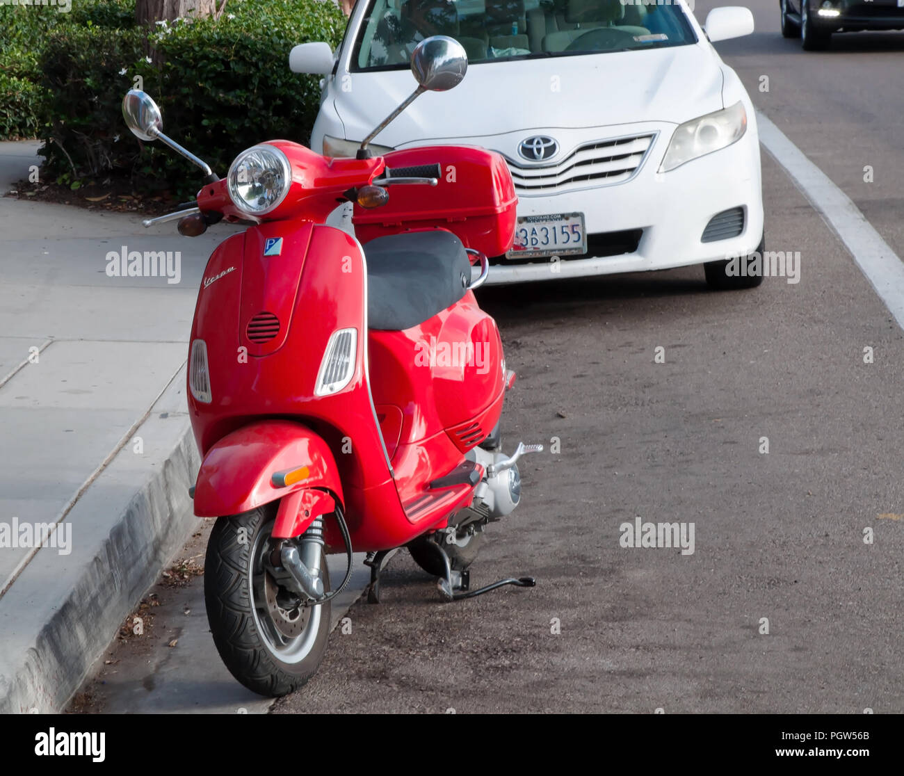 Un rosso scooter Vespa parcheggiata di fronte un bianco auto sulla strada in Encinitas, CALIFORNIA, STATI UNITI D'AMERICA Foto Stock