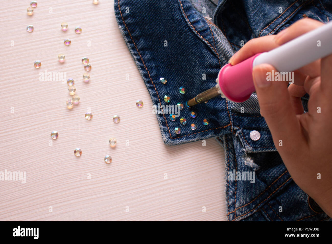 Decorazione a mano. Un processo di saldatura strass sul colletto di una camicia di denim da saldatore Foto Stock