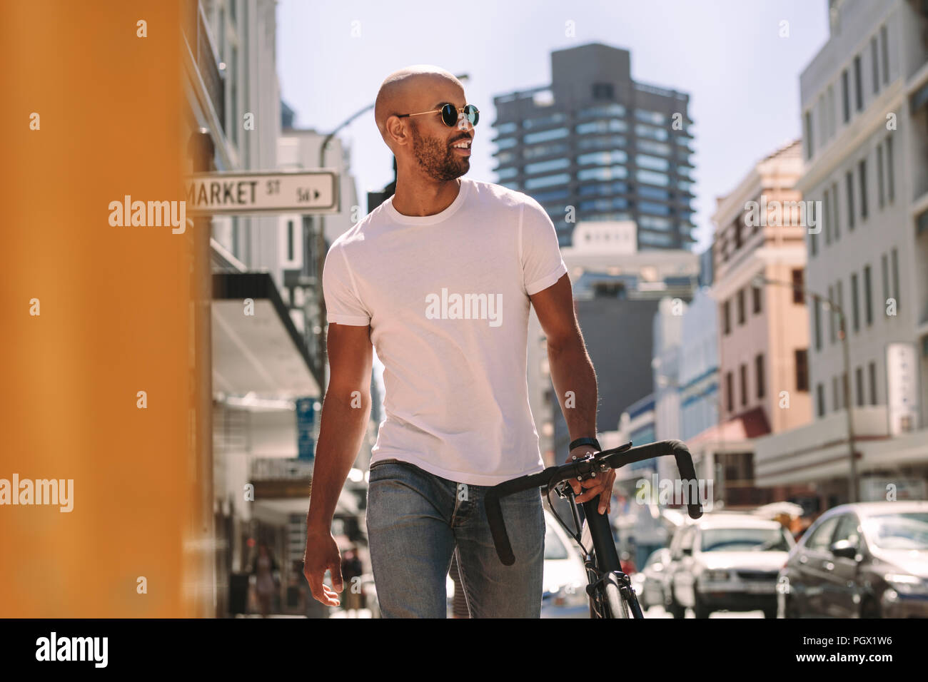 Bel giovane in casuals camminando per la strada con una bicicletta. L'uomo africano in casuals passeggiate all'aperto in città con una bici. Foto Stock