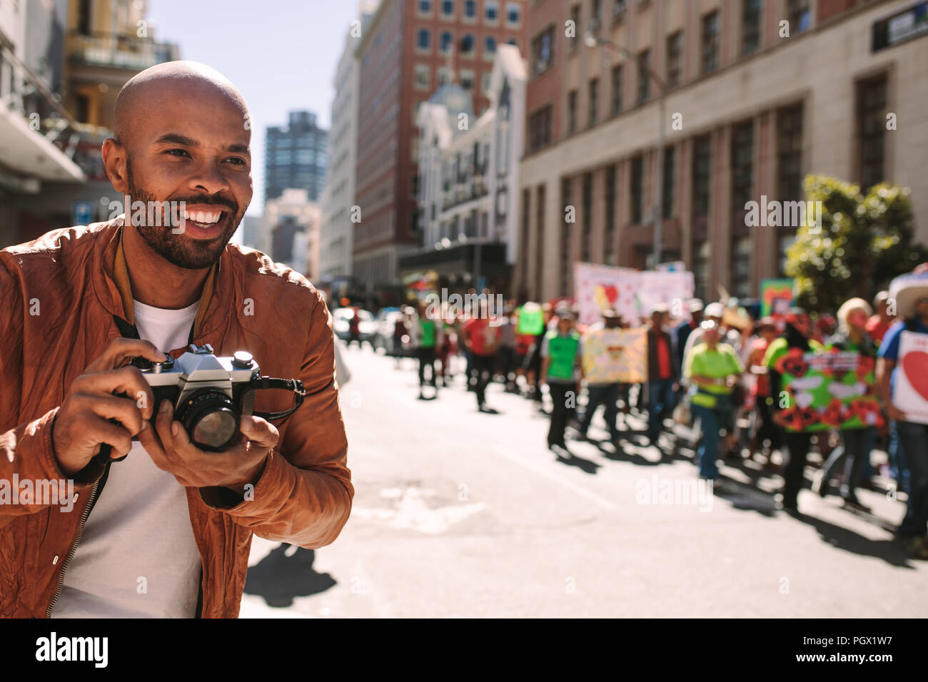 Sorridente fotografo africano prende le immagini di attivisti su strada. L'uomo prendendo le fotografie delle persone che camminano in un rally su strada della citta'. Foto Stock