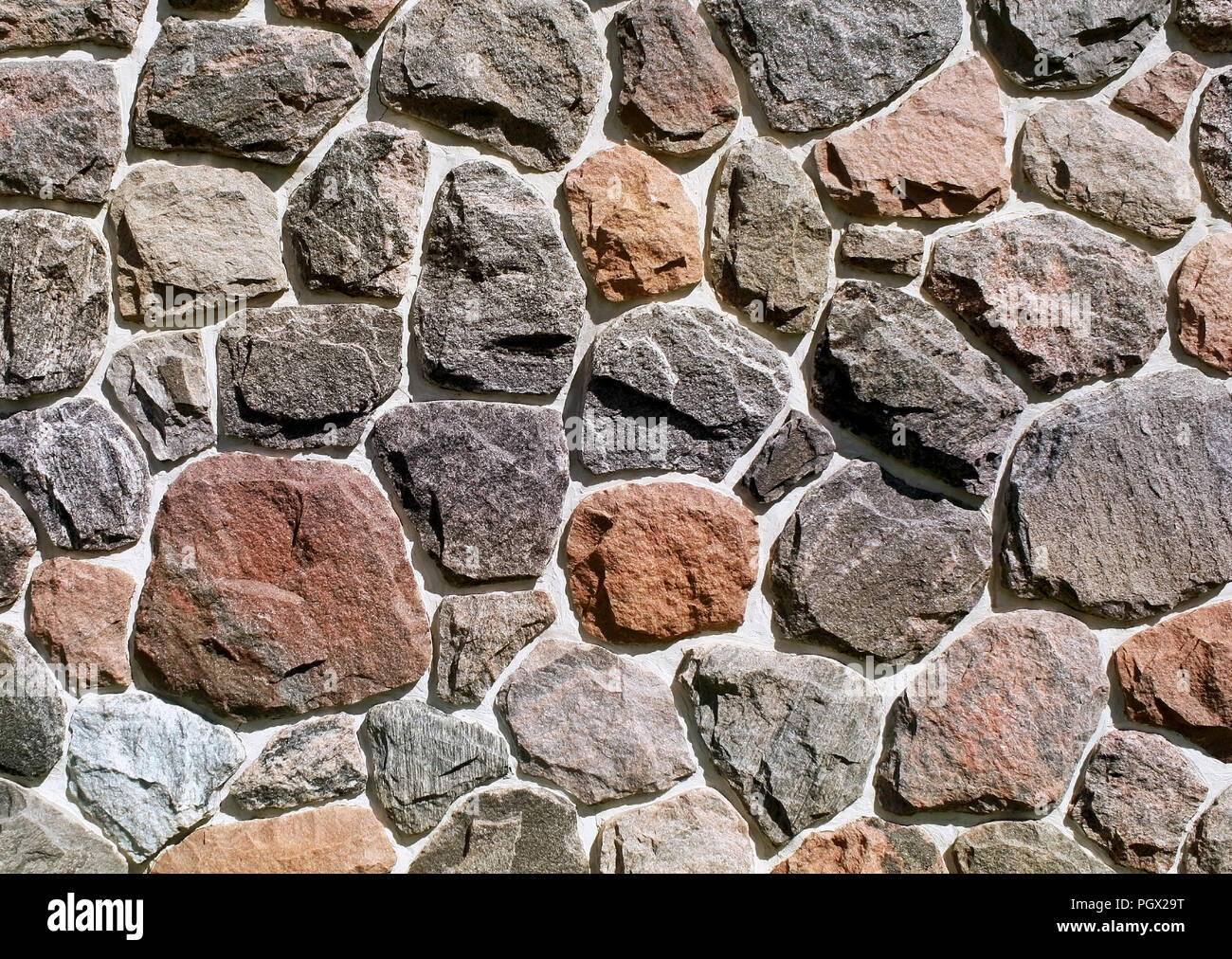 Un assortimento di rocce di diverse dimensioni e colori annegato nel calcestruzzo su un lato esterno della parete di roccia Foto Stock