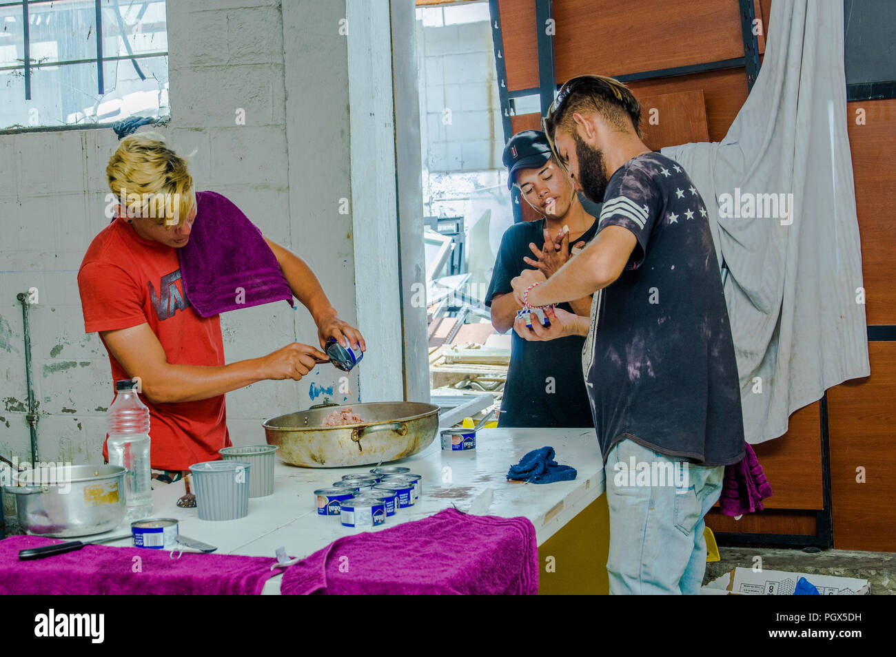 QUITO, ECUADOR, Agosto 21, 2018: Amici in cucina cucina la cena e aprire molte tonno può, all'interno di un rifugio per il popolo venezuelano che sfuggito f Foto Stock