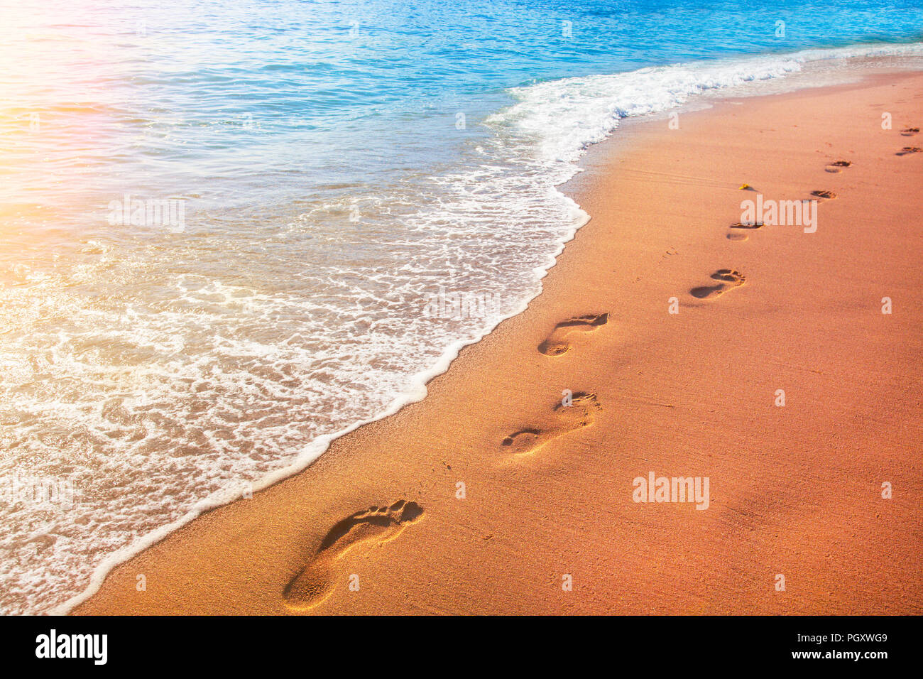 Spiaggia, onde e impronte in tempo al tramonto Foto Stock