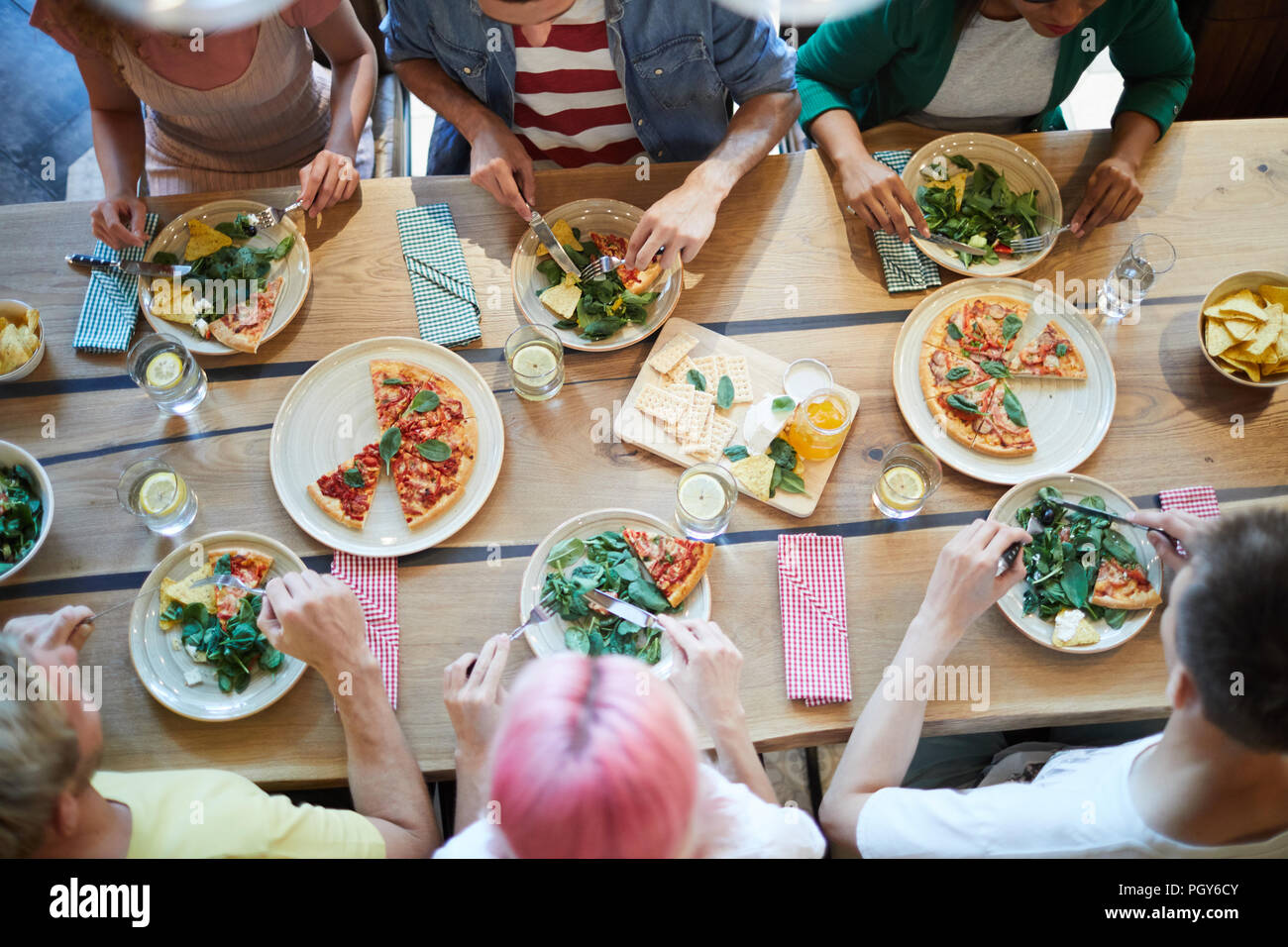 Panoramica di cibi gustosi serviti sul tavolo di legno e più giovani gente amichevole seduti intorno e a pranzo Foto Stock