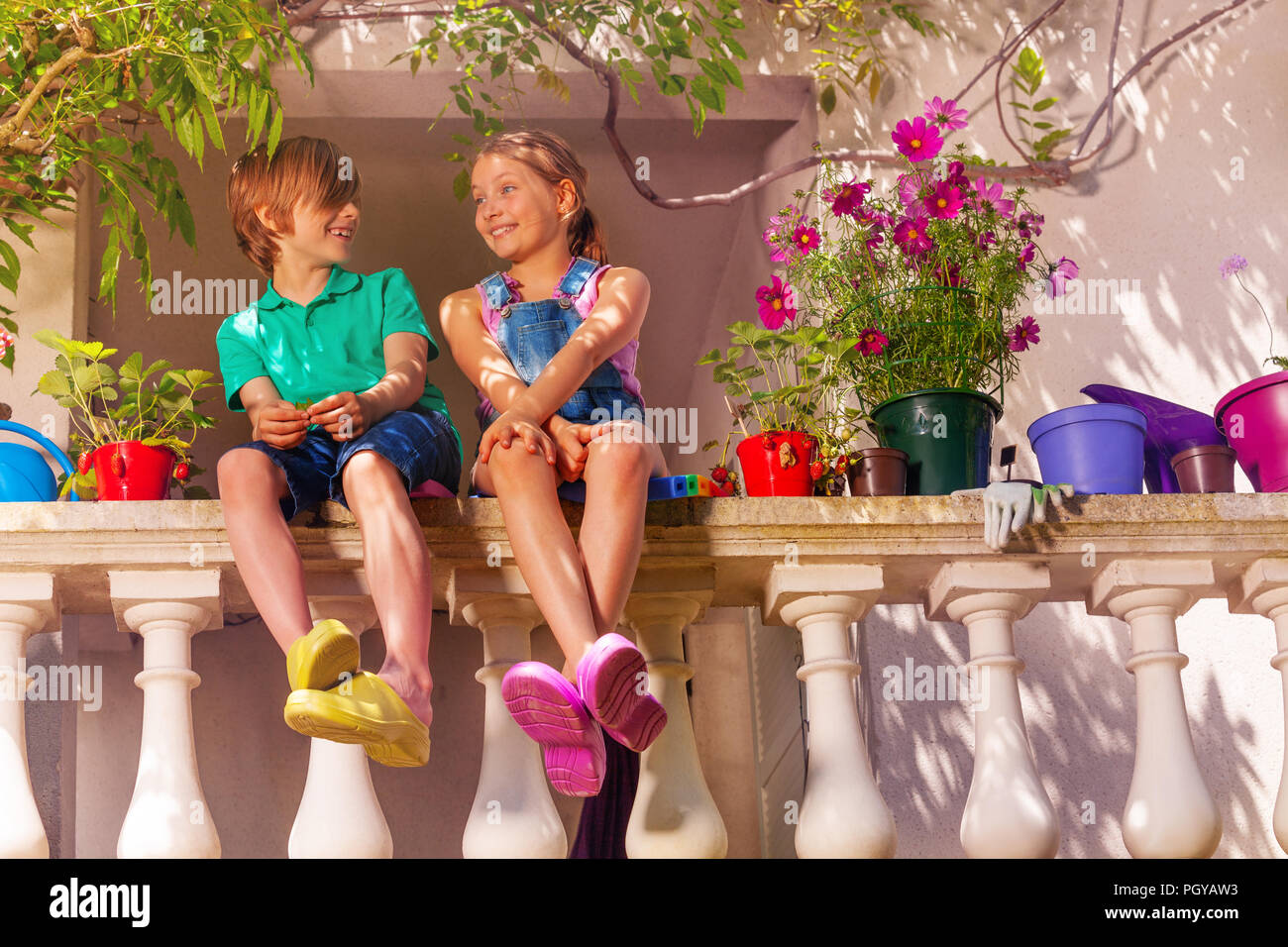 Inquadratura dal basso di felice preteen un ragazzo e una ragazza seduti sulla terrazza balaustrata tra vasi di fiori Foto Stock