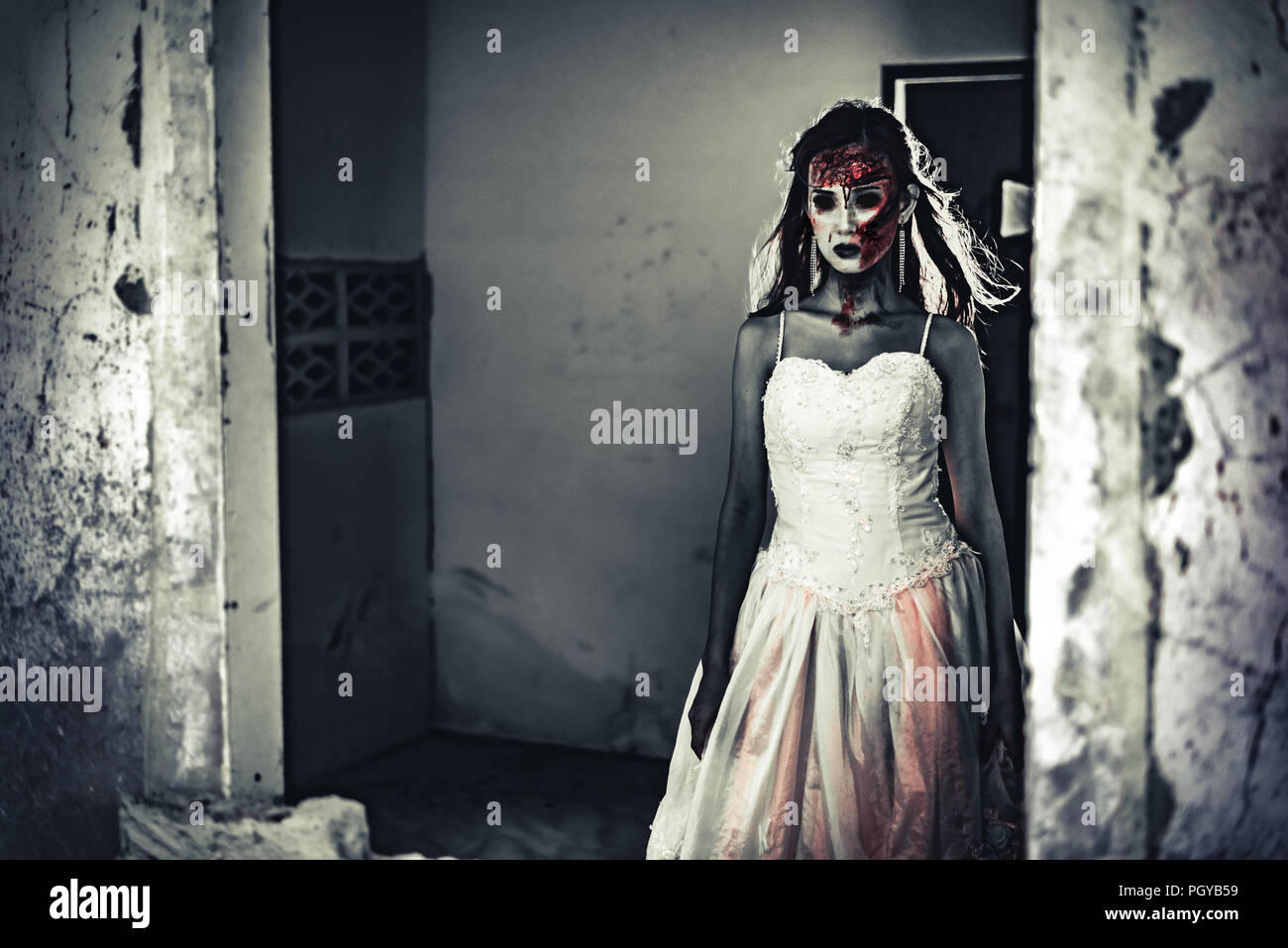 Femmina zombie cadavere in piedi nella parte anteriore della parete di grunge in casa abbandonata. L' orrore e la nozione di Ghost. Halloween day festival e il film spaventoso tema. Haun Foto Stock