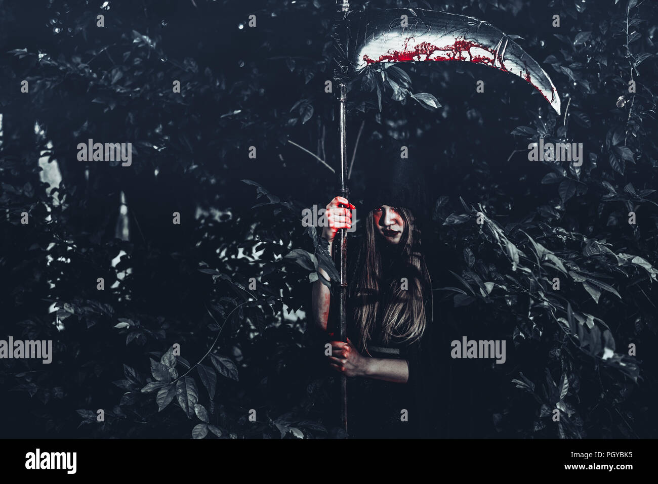 Demone femminile strega con sanguinosa reaper in piedi nella parte anteriore del mistero sullo sfondo della foresta. Halloween e la concezione religiosa. Demon angel e tema di Satana. Foto Stock