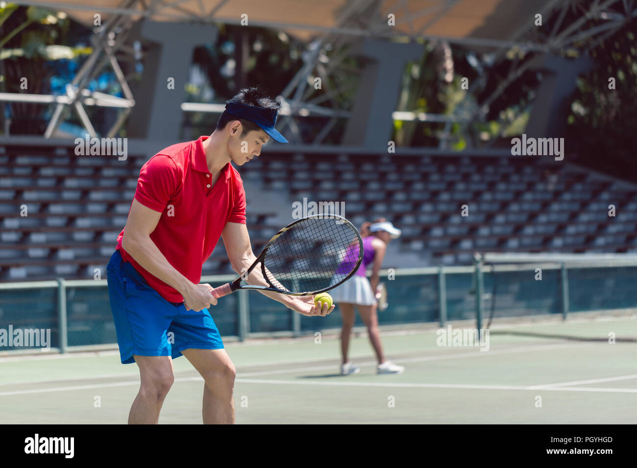 Vista laterale di un asiatico giocatore di tennis pronto a servire all'inizio di un doppio misto corrispondenza su un Professional tennis Foto Stock