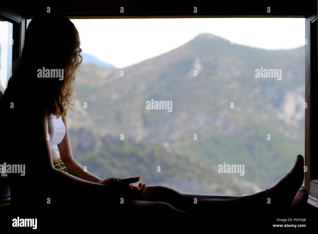 Ragazza seduta in una finestra guardando il paesaggio montuoso, Pirenei, Catalogna, Spagna. Foto Stock