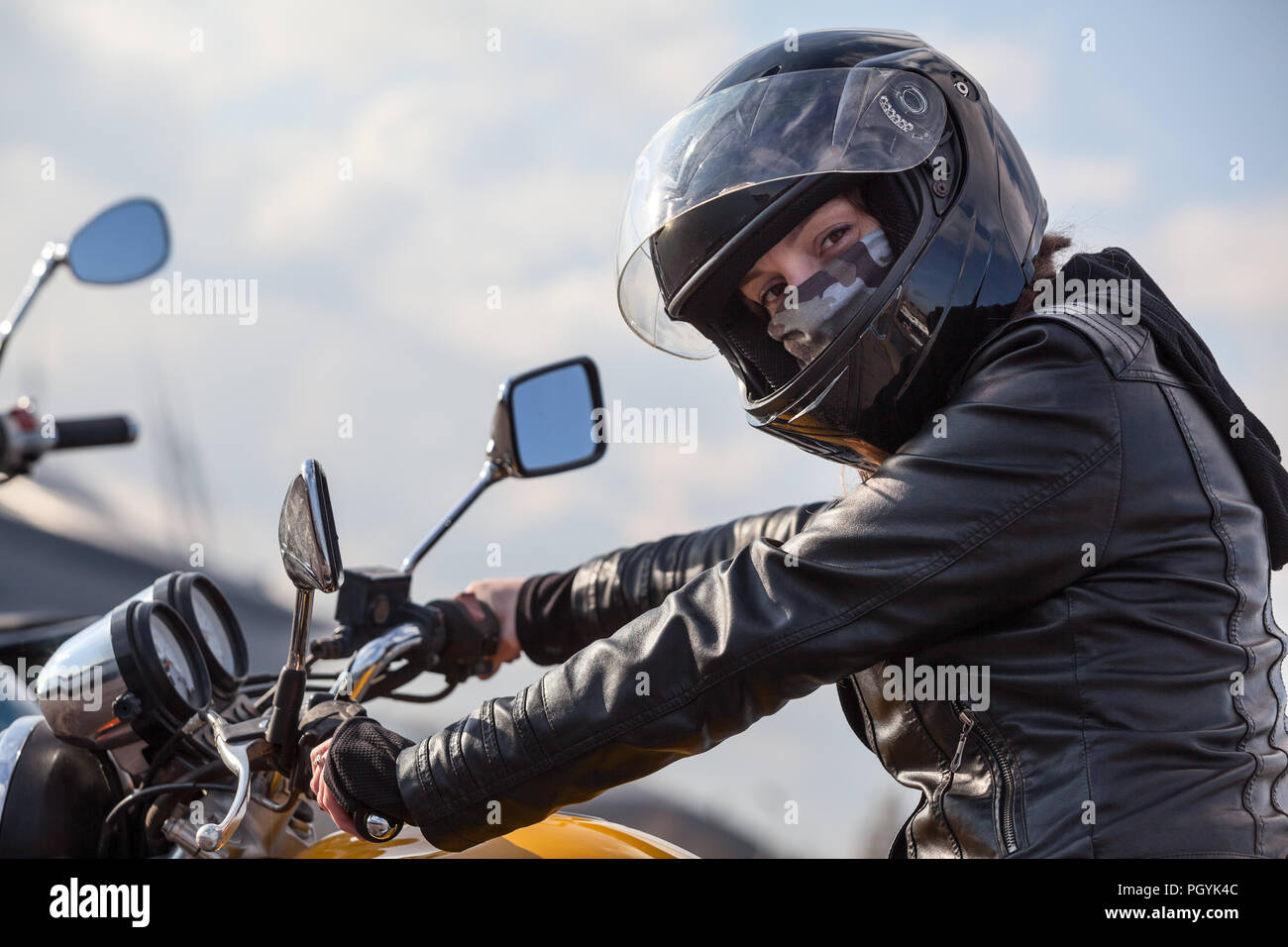 Conducente del motociclo in abito nero tiene il volante e guardando la telecamera, donna caucasica Foto Stock