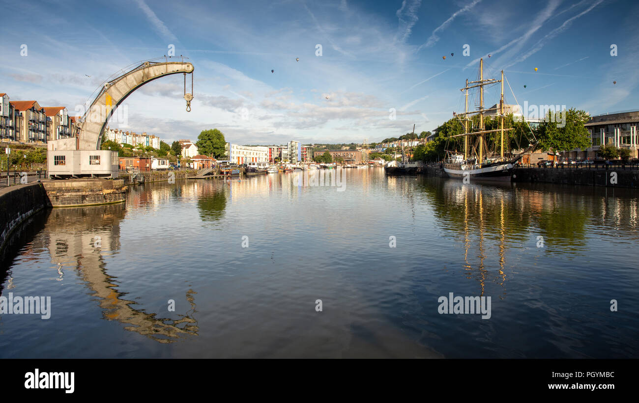 Bristol, Inghilterra, Regno Unito - 11 agosto 2018: i palloni ad aria calda di volare al di sopra di una tradizionale gru a vapore e tall ship in Bristol's Floating Harbour all'alba assortiti Foto Stock