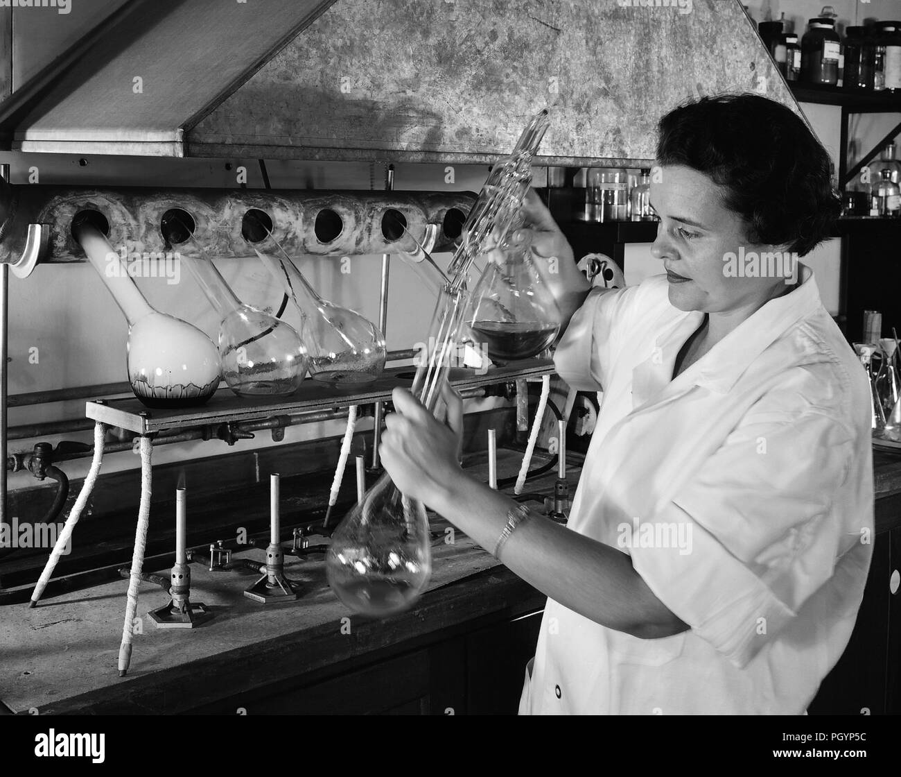 Fotografia in bianco e nero di laboratorian Ms Janet Spillane, effettuare una determinazione del tenore totale di azoto contenuto in un campione di compost di rifiuti, con un gran numero di bicchieri di vetro, bruciatori, e altri apparecchi scientifici visibile sullo sfondo, immagine cortesia CDC, 1958. () Foto Stock