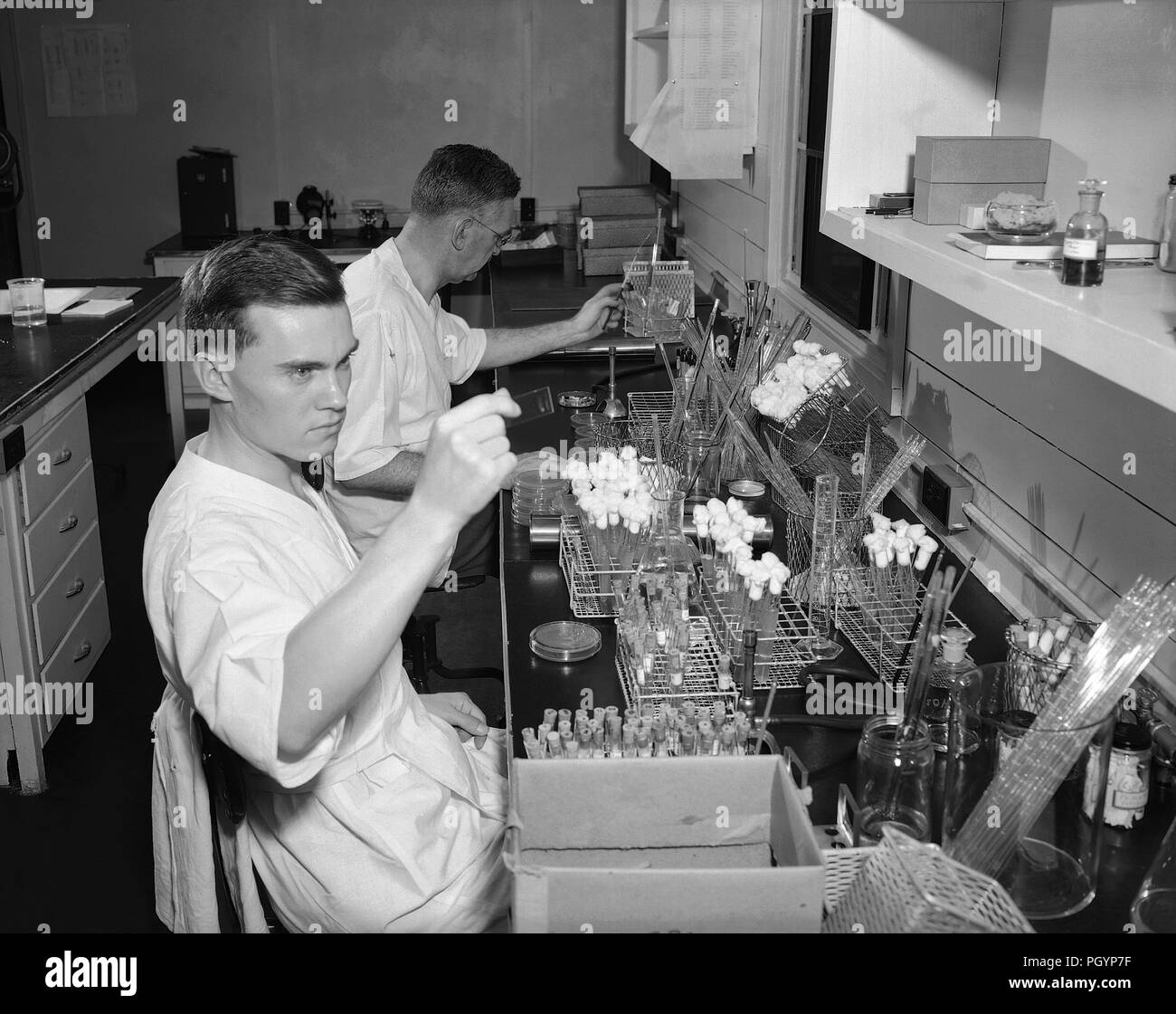 Fotografia in bianco e nero di Dr PR Edwards di noi servizio sanitario pubblico (fondo) e George Herman (in primo piano) alloggiata nell'enterico unità di batteriologia, laboratorio di eseguire uno studio incentrato su organismi batterici noti per provocare malattie gastrointestinali, compresa la diarrea e dissenteria, con un gran numero di fiale di vetro visibile sul tavolo di fronte a loro, fotografata nel 1948 circa al 1963, Immagine cortesia CDC, 1980. () Foto Stock