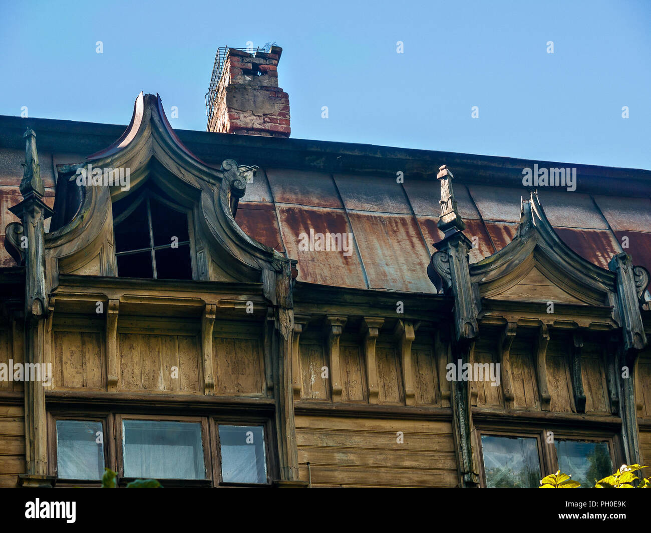 Sotto il tetto coperto del vecchio e storico casa in legno di colore giallo nella città di San Pietroburgo, ci sono abilmente eseguiti finestra e soffitta tri Foto Stock