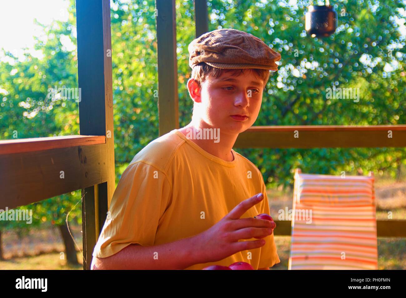 Il ragazzo è seduto su una veranda e eatting mele fresche. Sognante e immagine romantica. Estate e infanzia felice concetto Foto Stock