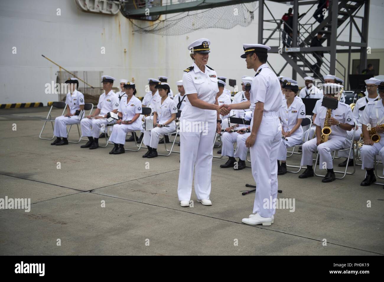 TOKYO (16 giugno 2018) -- STATI UNITI Navy Lt. Kelly Cartwright, conduttore di U.S. Flotta del Pacifico Band, scuote le mani con il Giappone marittimo Forza di Autodifesa (JMSDF) Tenente j.g. K. Honda, conduttore della JMSDF Yokosuka banda, come le bande di giocare insieme durante una cerimonia di benvenuto per i militari di comando Sealift nave ospedale USNS misericordia (T-AH 19) dopo l'arrivo della nave in Tokyo. La misericordia è rendere visite porta a Yokosuka e Tokyo per promuovere le relazioni tra gli Stati Uniti I marinai della marina militare e cittadini giapponesi attraverso lo scambio culturale e di formazione bilaterali. Foto Stock