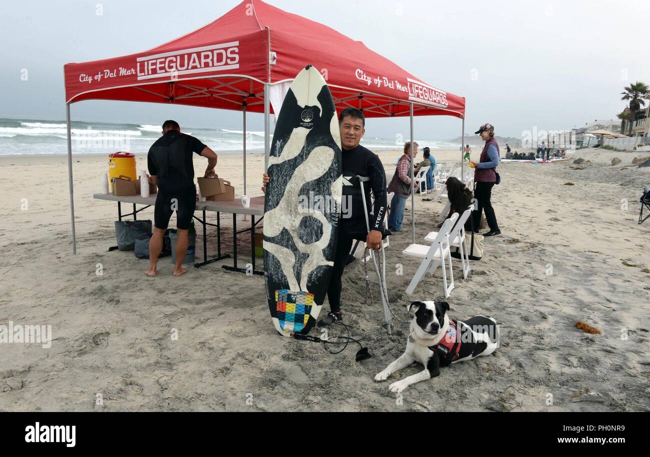 DEL MAR, California (14 giugno 2018) Marine Corps veterano Chris piccolo posano con il suo nero-e-bianco surfboard personalizzato per corrispondere con il suo cane terapia Sofi prima di navigare con altri pazienti da Naval Medical Center di San Diego (NMCSD) Surf clinica. Il giorno segnato anche NMCSD Surf Clinic del decimo anniversario. La clinica è coordinato dalla salute e wellness reparto per riabilitare i feriti e ammalati e feriti i membri del servizio tramite esercizi e terapia di ricreazione per migliorare il loro livello di funzione e di mobilità e mentale ben-essere. Foto Stock