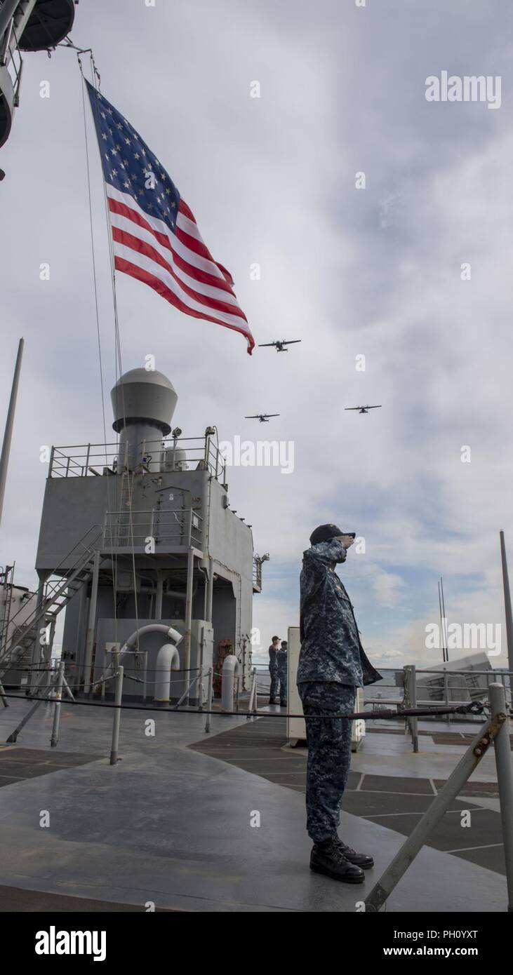 La Polonia (24 giugno 2018) Chief Operations Specialist Reginald Washington rende onora come il Polacco Aeromobili sorvolano il harpers Ferry-class dock landing ship USS Oak Hill (LSD 51) durante una parata di navi in onore della Polonia di 100-anno anniversario navale, a Gdynia, Polonia, 24 giugno 2018. Oak Hill, homeported in Virginia Beach, Virginia, sta conducendo operazioni navali negli Stati Uniti Sesta flotta area di operazioni. Foto Stock