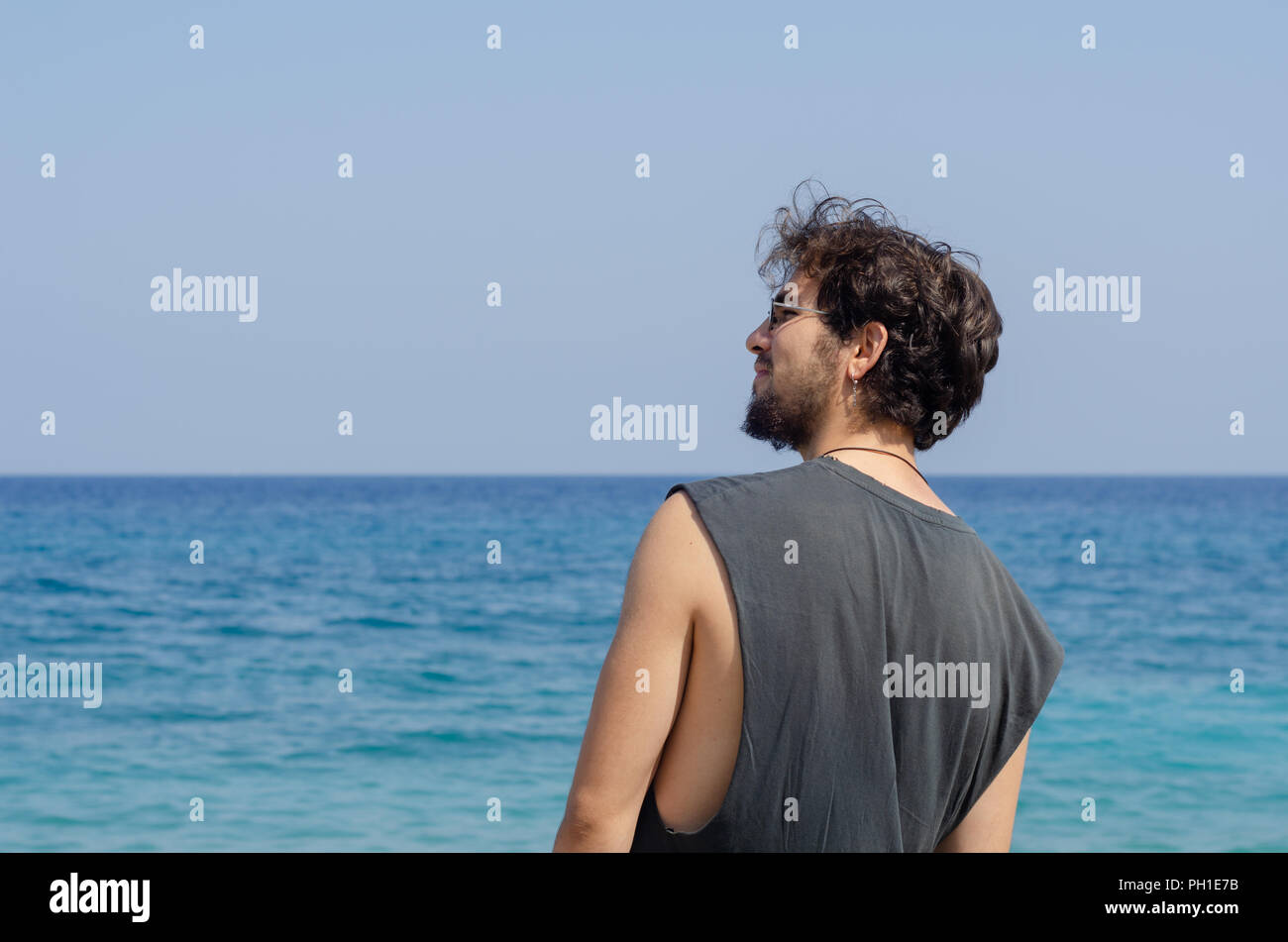 Barbuto giovane uomo che indossa un orecchino sorride davanti al mare  mentre cercano la sua sinistra e guardare avanti Foto stock - Alamy