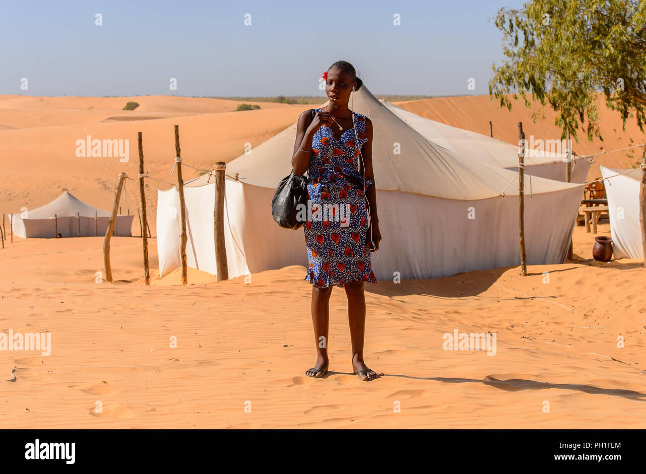 Deserto LAMPOUL, SENEGAL - Apr 23, 2017: Non identificato donna senegalese con trecce indossa la striscia rossa sul suo capo e abiti colorati contiene un sacchetto in una lampada Foto Stock
