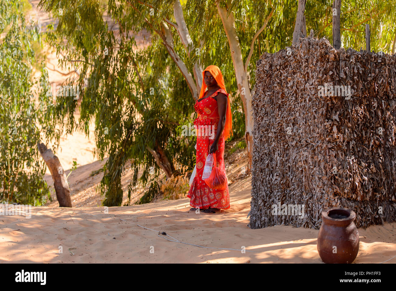 Deserto LAMPOUL, SENEGAL - Apr 23, 2017: Non identificato donna senegalese in rosso abiti tradizionali detiene un sacco e una bottiglia di acqua in un deserto Lampoul Foto Stock