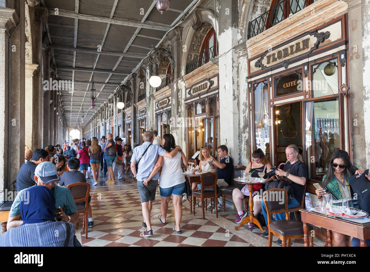 Persone a pranzo tavoli fuori in ombra sotto il porticato al Caffè Florian e Piazza San Marco, San Marco, Venezia, Veneto, Italia durante la European hea Foto Stock