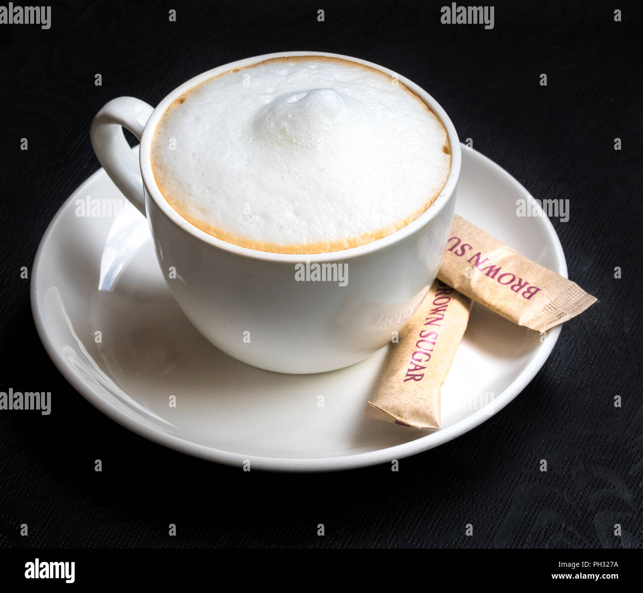 Una tazza di cappuccino caldo servito con zucchero di canna Foto Stock