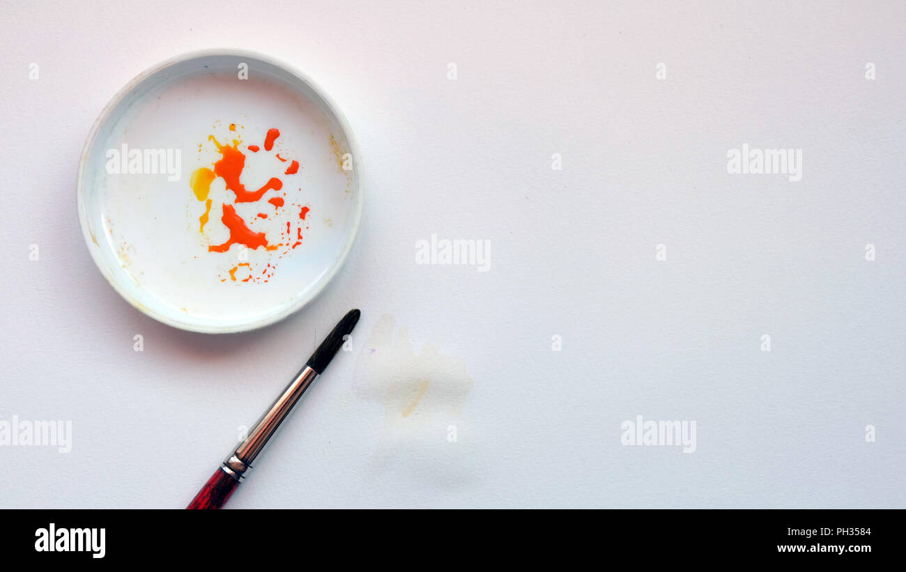Piatto di laici acqua spazzola di colore e una vaschetta di miscelazione con vernice arancione, su un libro bianco sullo sfondo Foto Stock