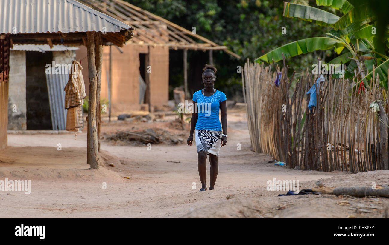 OUSSOUYE, SENEGAL - Apr 30, 2017: Non identificato donna senegalese in maglietta blu e mantello colorato cammina lungo la strada nel bosco sacro vicino Kaguit Foto Stock