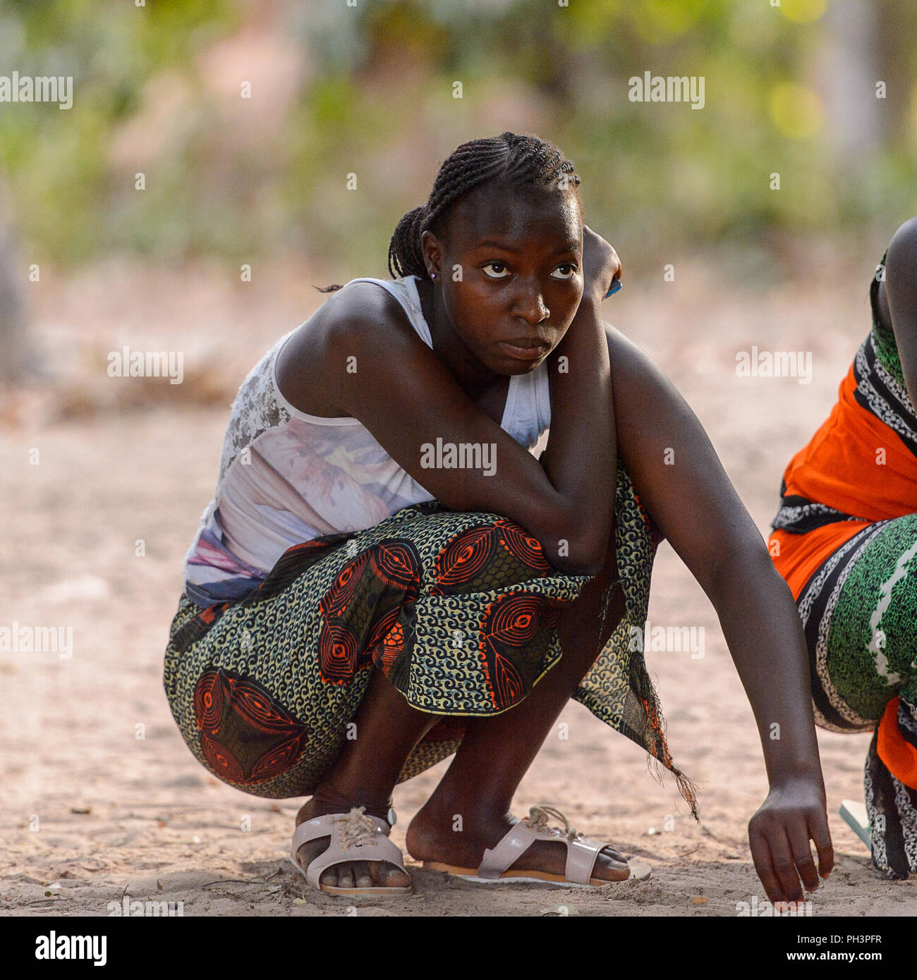 OUSSOUYE, SENEGAL - Apr 30, 2017: Non identificato donna senegalese con trecce squat nel bosco sacro vicino villaggio Kaguit Foto Stock