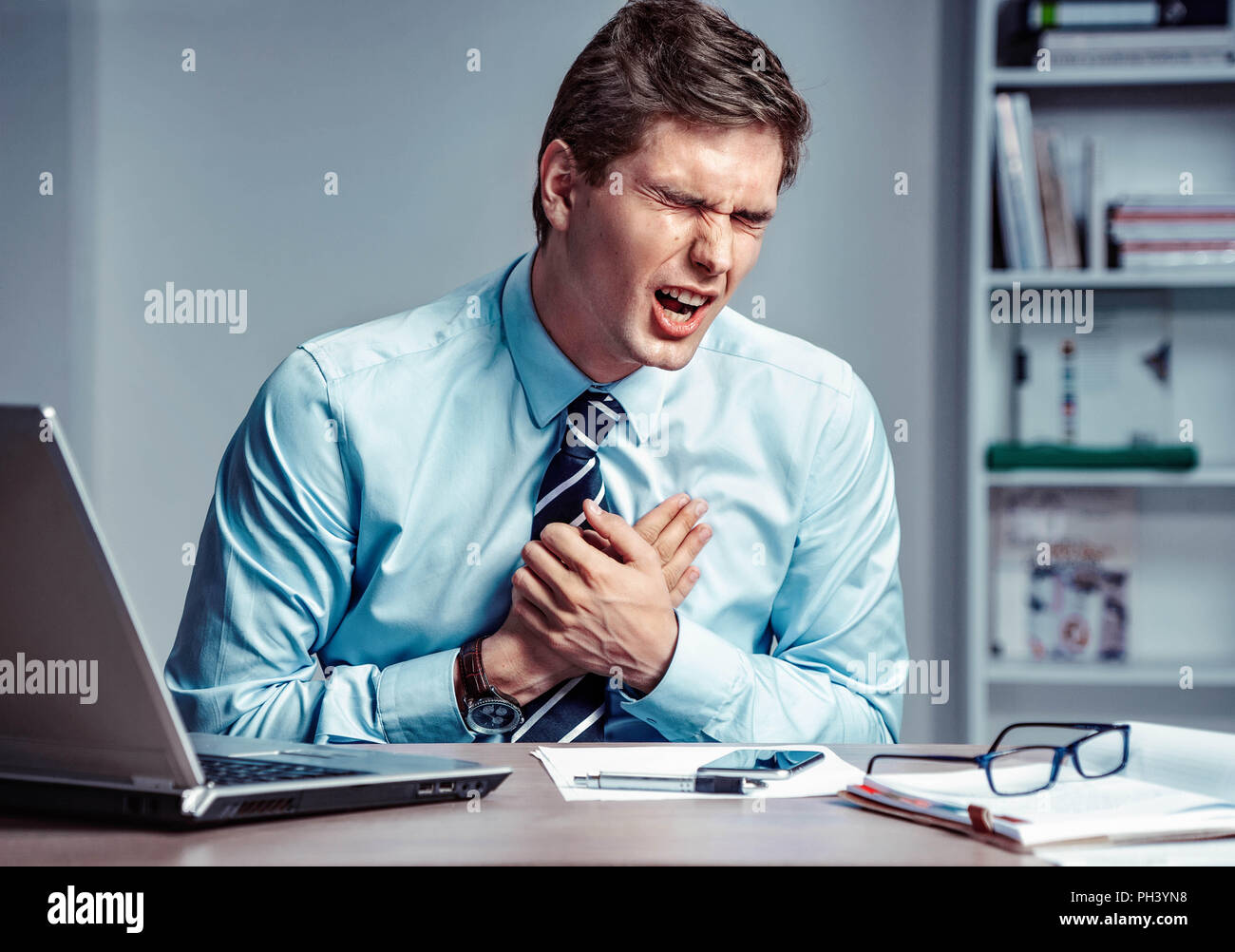 Office manager avente un attacco di cuore. Foto del giovane uomo tenendo una mano sul petto dolorosa nel luogo di lavoro. Concetto medico. Foto Stock