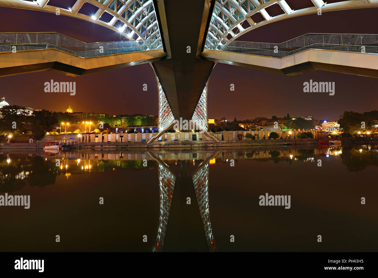 Riflessioni del moderno ponte pedonale noto come Ponte di Pace, oltre il fiume Mtkvari, notte a Tbilisi, Georgia Foto Stock