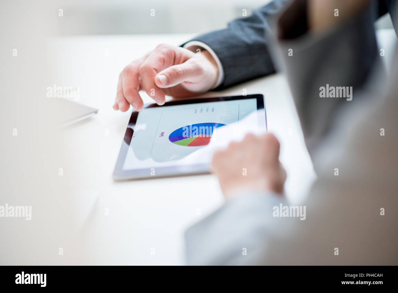 Imprenditore discutendo un analitico grafico a torta con un collega, vista ravvicinata della mano e il grafico su un tablet sopra la spalla del suo colleagu Foto Stock