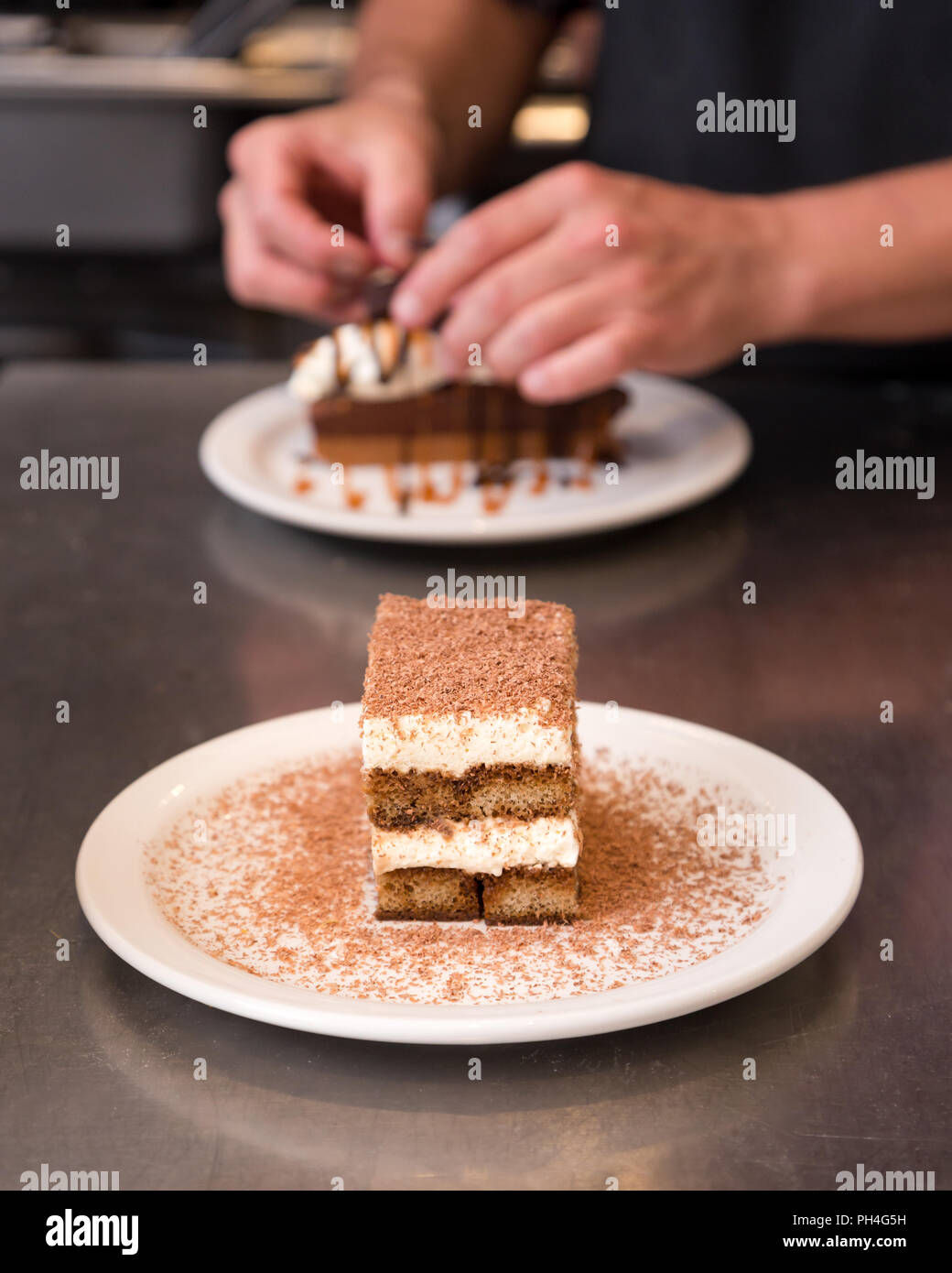 Il tiramisù spolverato di cioccolato con una torta al cioccolato in background. Foto Stock