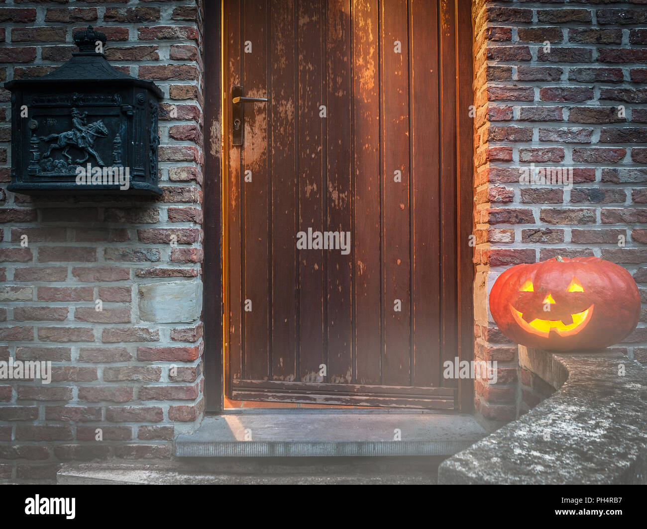 Una nebbiosa Halloween scena di una porta socchiusa, un ombra fantasma, un sorridente jackolantern e un trumpeting horseman su un antico cassetta postale. Foto Stock