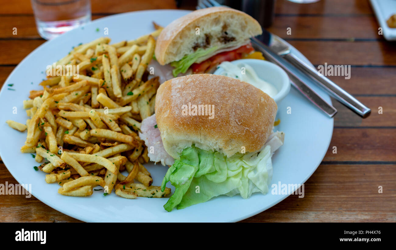 Sandwich al tonno sulla piastra bianca, visto dal di sopra, servito con patate fritte e salsa acidula, sul tavolo di legno, in un ristorante di impostazione Foto Stock