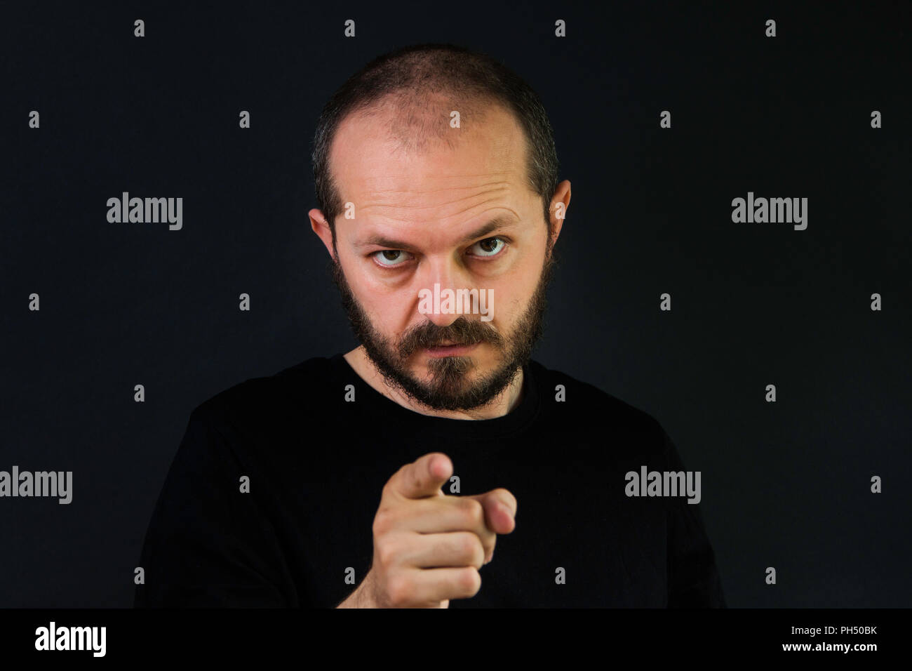 Uomo serio con la barba e mustaches su sfondo nero in chiave di basso, puntare il dito verso la telecamera Foto Stock