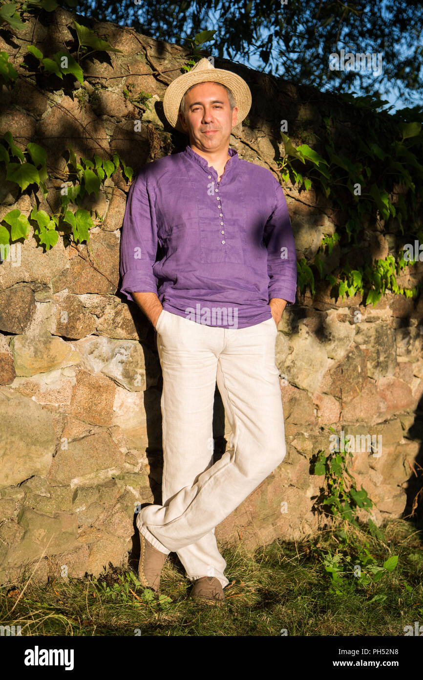 Uomo in camicia di lino e cappello di paglia sorge vicino al muro di pietra  Foto stock - Alamy