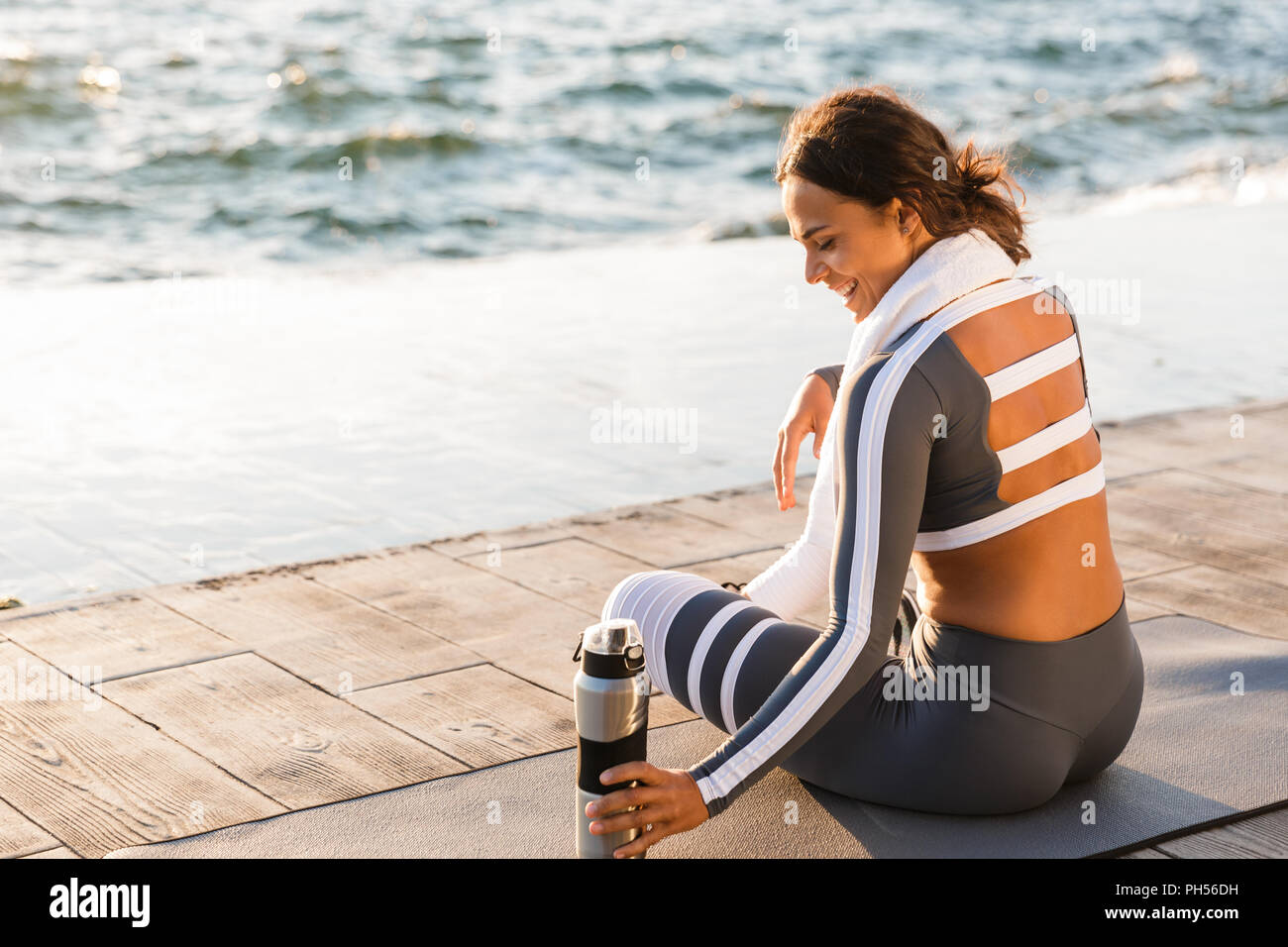 Immagine della giovane e bella donna fitness all'aperto sulla spiaggia hanno un resto seduta con asciugamani e acqua. Foto Stock