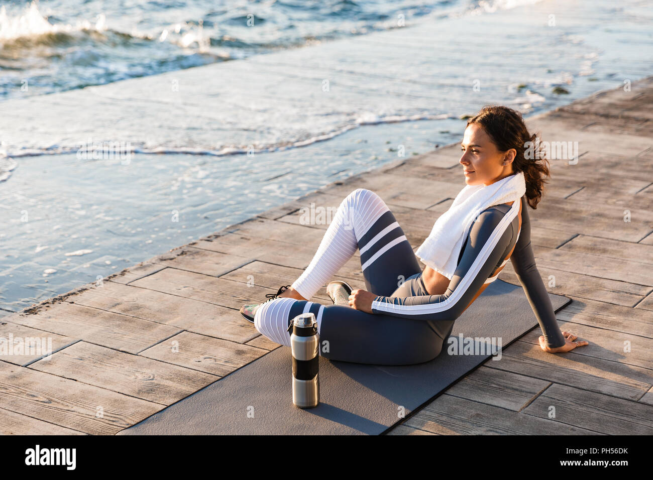 Immagine della giovane e bella donna fitness all'aperto sulla spiaggia hanno un resto seduta con asciugamani e acqua. Foto Stock