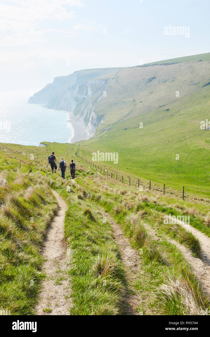 Un gruppo di tre persone a piedi in discesa su una banca erbosa su una soleggiata giornata chiara, nei pressi di porta di Durdle su Jurassic Coast del Sud Inghilterra Foto Stock