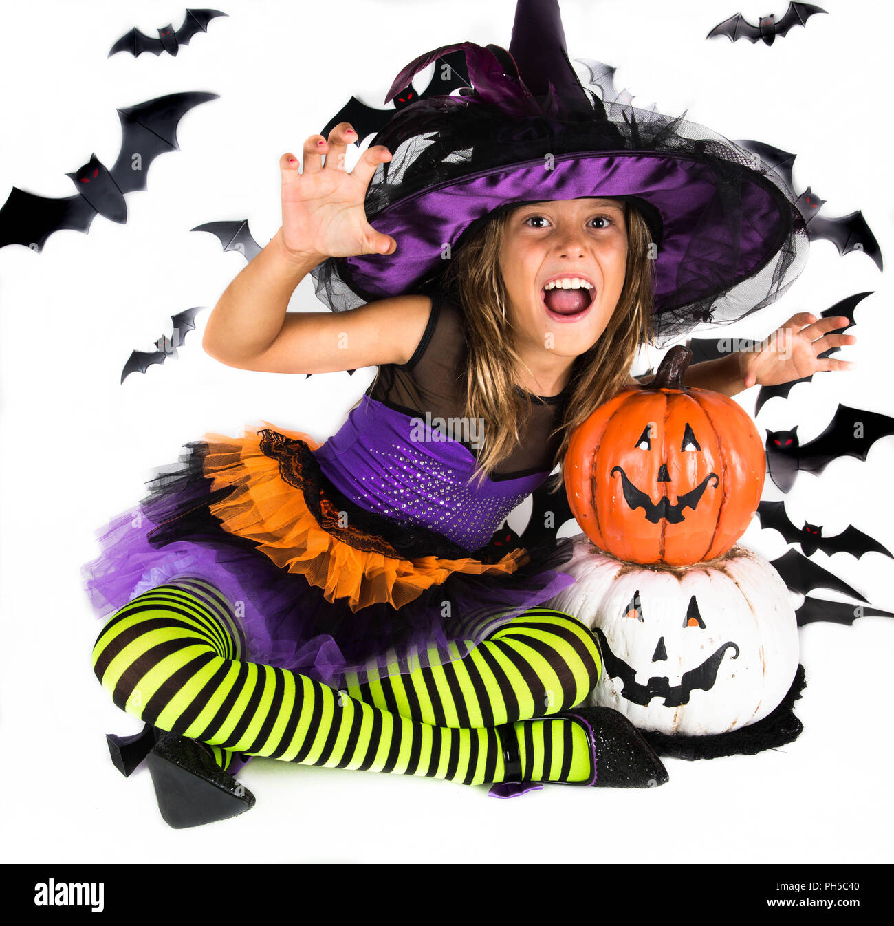 Happy Halloween strega & felice di zucca. Bambina con un costume di Halloween di una strega con cappello, striped gambe tenendo due smiley zucche di Halloween Foto Stock