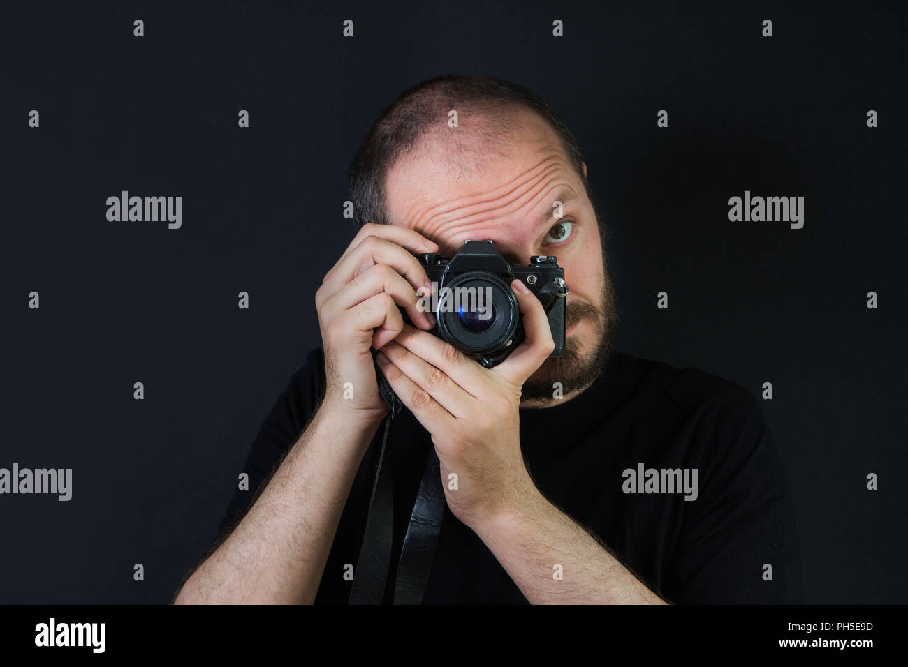 Uomo su sfondo nero in chiave di basso, tenendo la telecamera analogica e scattare foto Foto Stock