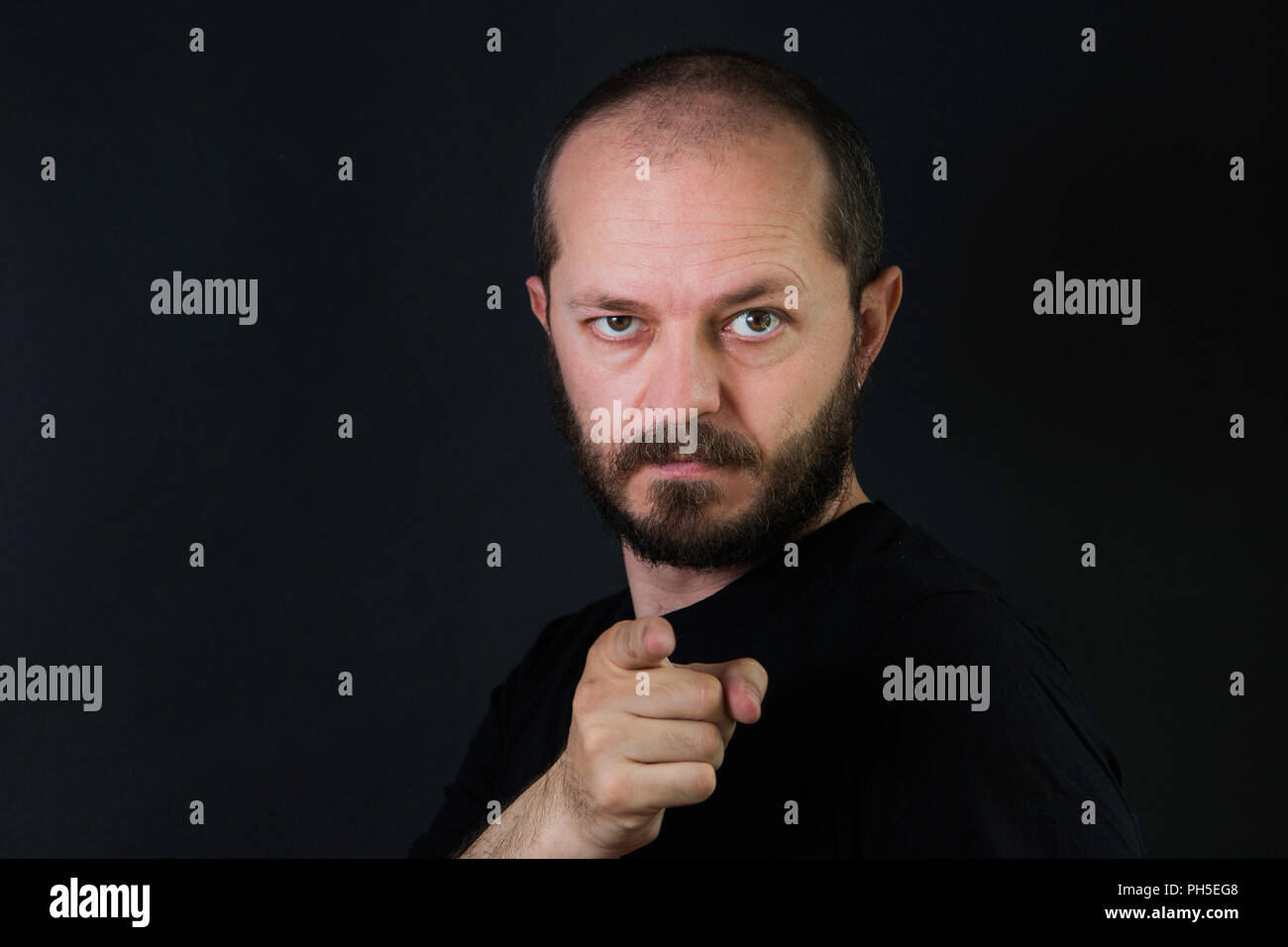 Uomo serio con la barba e mustaches su sfondo nero in chiave di basso, puntare il dito verso la telecamera Foto Stock