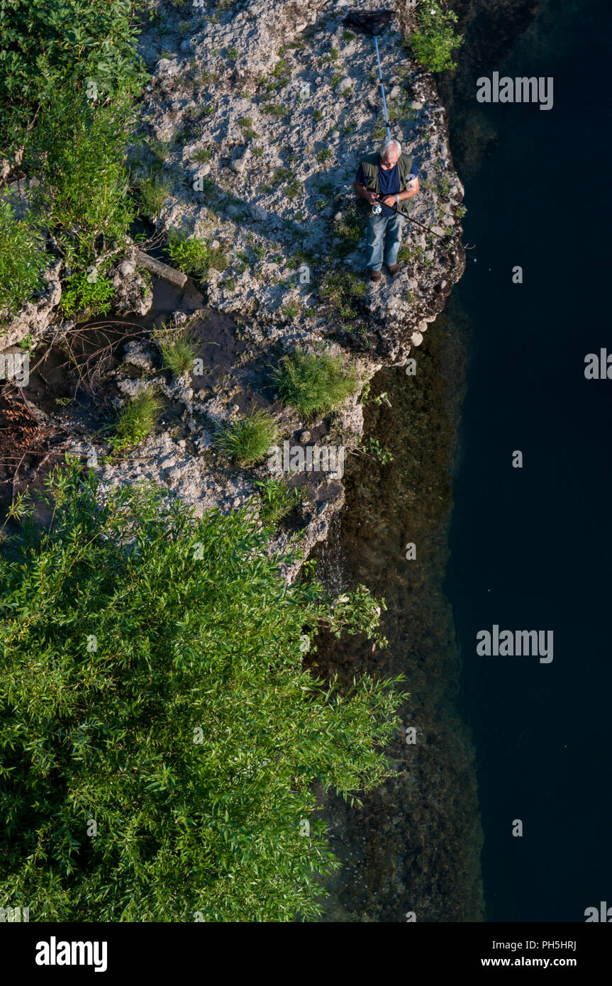 La Bosnia, l'Europa: veduta aerea di un pescatore con la canna da pesca su una roccia la pesca nelle verdi acque del fiume Neretva a Mostar Foto Stock