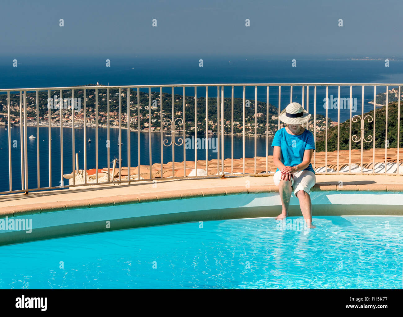 La donna il raffreddamento i suoi piedi in una piscina con i paesi del Mediterraneo e del Cap Ferrat in background Foto Stock