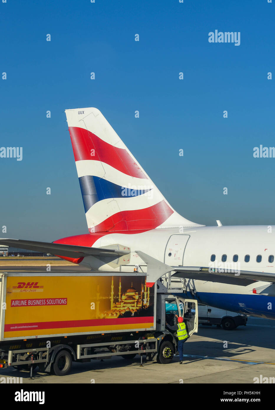 Pinna di coda di un British Airways Airbus A320 jet all'aeroporto di Londra Heathrow. Un carrello con DHL la pubblicità è il caricamento di catering. Foto Stock