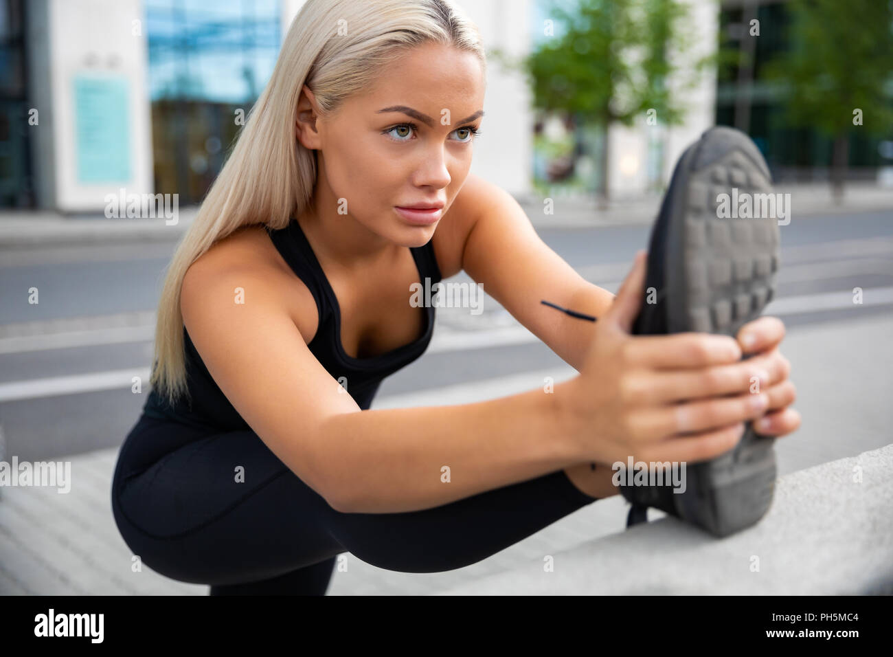 Determinata la donna facendo esercizio di stretching alla ringhiera sul marciapiede Foto Stock